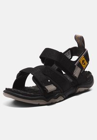 Svarta sandaler med flera justerbara remmar i texturerad tyg, vadderad sula och gummisula med ett greppvänligt mönster.