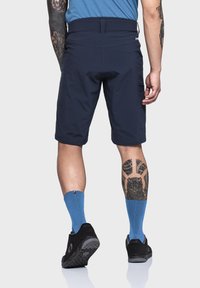 Marineblaue Shorts mit glatter Textur, flachem Bund und Seitentaschen. Kombiniert mit blauen Socken und schwarzen Schuhen, die Beintattoos zur Schau stellen.