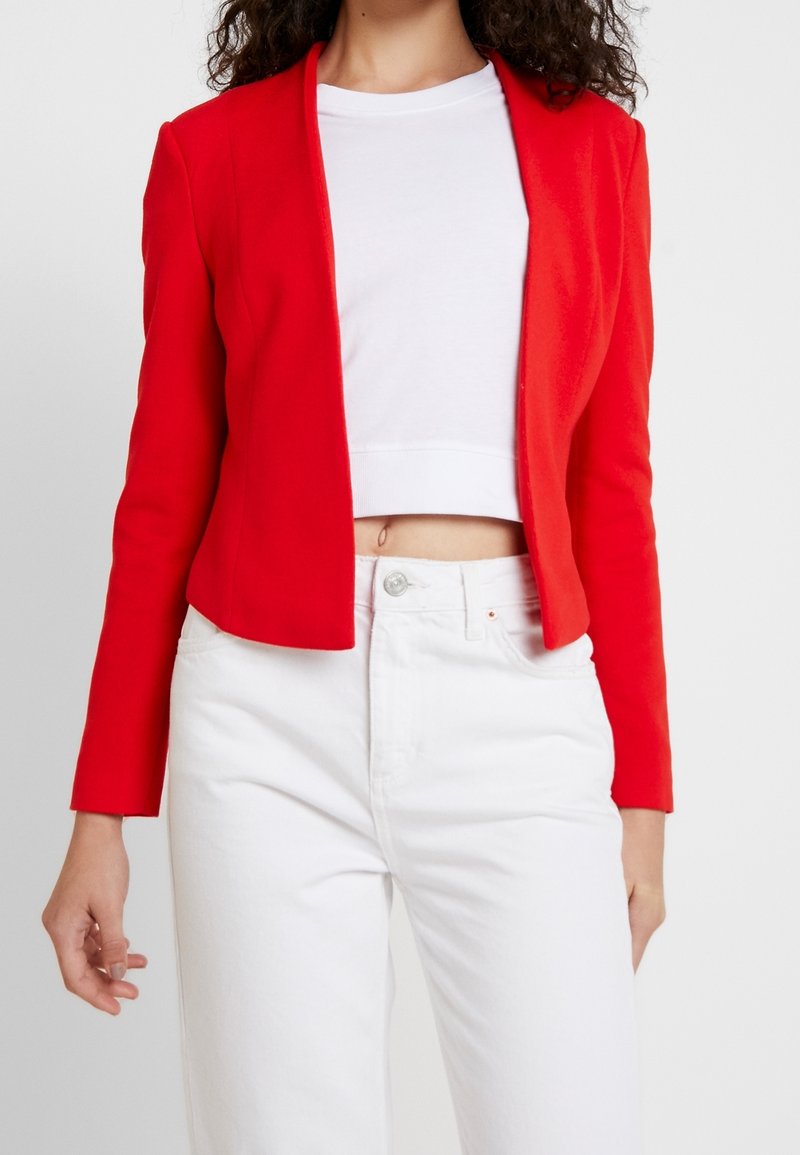 Rode getailleerde blazer met lange mouwen, ingesneden revers en een gladde textuur, gecombineerd met een witte cropped shirt en hoge taille witte jeans.