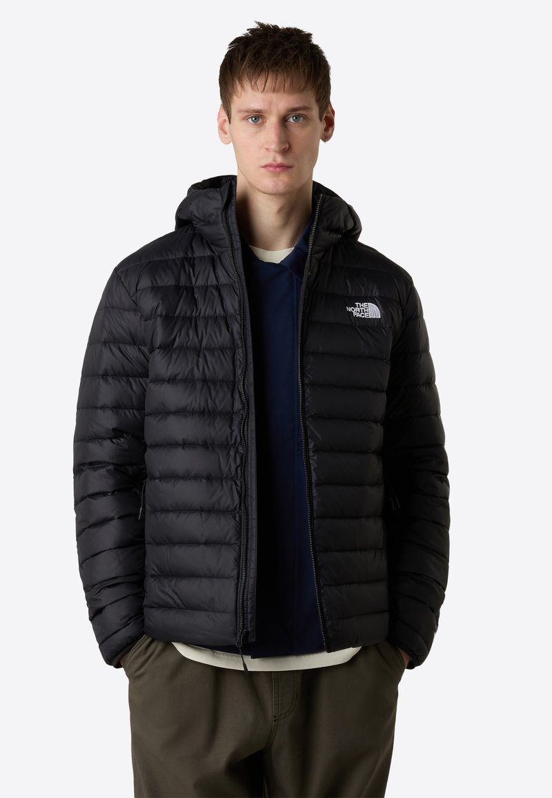 Black, puffy insulated jacket with a hood, featuring a full zipper, side pockets, and a logo on the left chest. Smooth texture, quilted design.