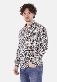 Camicia a maniche lunghe bianco e nero con motivo, dotata di colletto, decorata con dettagli floreali e bottoni, dal fit rilassato. Indossati jeans di denim casual.