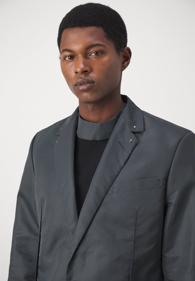 Grauer Blazer mit glatter Textur, einer Einzelne Tasche und Stehkragen. Verfügt über ein minimalistisches Design und subtile Hardwareakzente.