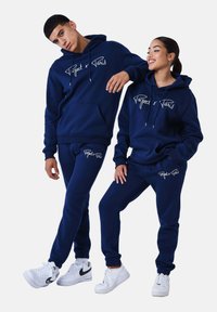Sudaderas con capucha y pantalones deportivos azul marino con texto blanco "Project x Paris". El material es suave, con un corte holgado y cordones ajustables.