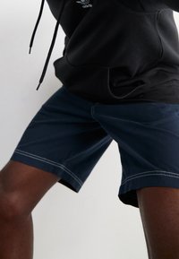 Pantalones cortos azul marino con costuras claras contrastantes, hechos de una tela suave. Presentan una cinturilla elástica y un corte relajado.