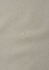Tissu beige clair avec une surface texturée, présentant de nombreuses petites gouttes d'eau, illustrant ses propriétés imperméables.