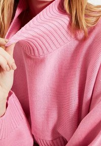 Gebreide roze trui met een geribbelde hoge kraag en brede mouwen, die een gestructureerde stof met een losse pasvorm toont.