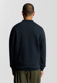 Donker marineblauw sweatshirt met een ronde hals, raglanmouwen en geribbelde manchetten. Het materiaal lijkt zacht en textuur te hebben, gedragen met olijfgroene broek.
