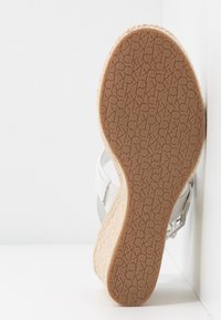 Sandale espadrille avec une semelle en jute tressé et une semelle extérieure en caoutchouc brun texturé, dotée de brides en cuir blanc et d'un design de talon plat.