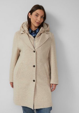 Beige Mantel mit Kapuze, strukturierter Schnitt, Ein-Knopf-Verschluss, Seitentaschen und strukturiertem Stoff. Über einem karierten Hemd getragen.