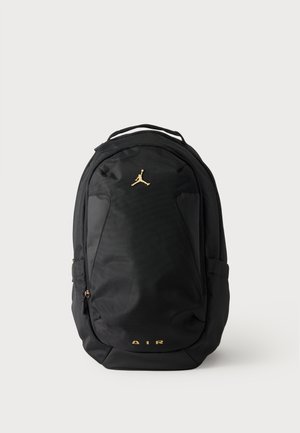 Μαύρο σακίδιο πλάτης με χρυσλό λογότυπο Jumpman κοντά στην κορυφή και χρυσλό κείμενο "AIR" κοντά στο κάτω μέρος, με μπροστινή τσέπη με φερμουάρ και πλαϊνές θήκες.