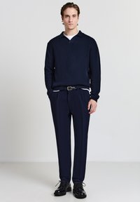 Dunkelblauer gerippter Strickpullover mit Kragen, kombiniert mit passenden maßgeschneiderten Hosen und schwarzen Schnürschuhen. Einfaches und modernes Design.