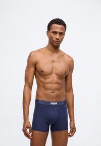 Μπλέ σλιπ μποξέρ με ελαστική μέση που φέρει το λογότυπο "PUMA". Στενή εφαρμογή και απαλό βαμβακερό υλικό. Το μοντέλο στέκεται με αυτοπεποίθηση.