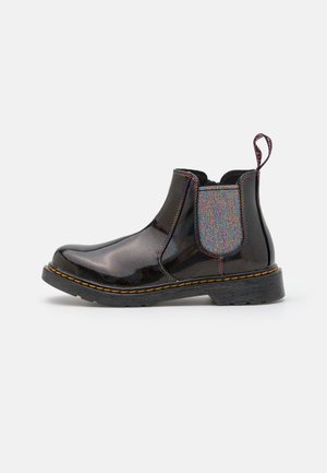 Blank sort Chelsea-støvle med iriserende elastisk sidepanel, gule syninger på sålen og stofstrop i hælen på hvid baggrund.