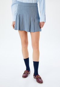 Falda plisada de color azul claro con una tela texturizada, combinada con calcetas de rodilla en navy y mocasines burdeos con acentos dorados.