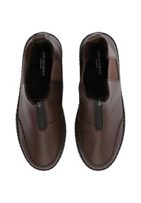 Zapatos de cuero marrón con una cremallera en la parte frontal, paneles laterales elásticos y suelas de goma texturizada. Forro negro suave visible en el interior.