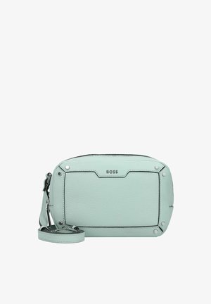 Hellmintgrüne BOSS Leder-Crossbody-Tasche mit Reißverschluss, Detail im vorderen Bereich und verstellbarem Gurt, der neben der Tasche zusammengerollt liegt.