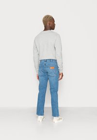 Grijze long-sleeve shirt gecombineerd met lichtblauwe denim jeans. De jeans hebben een achterpatch en een klassiek vijf-pocket ontwerp. Witte sneakers maken de look compleet.