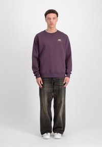 Lilla sweatshirt med rund halsudskæring og ribbede manchetter, parret med løse, slidte sorte jeans, båret med hvide sneakers.