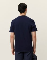 J�ūras zila kokvilnas t-kreklu ar klasisku apaļu kakla izgriezumu un īsām piedurknēm, skatīts no aizmugures, ar gludu tekstūru.