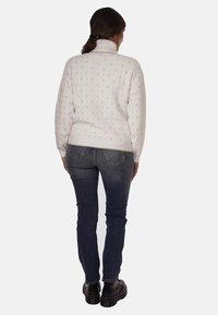 Maglione bianco lavorato a maglia con colletto alto, caratterizzato da un sottile motivo a rombi. Abbinato a jeans aderenti blu scuro e scarpe nere con suola spessa.
