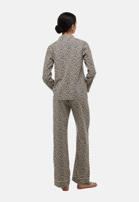 Ensemble de pyjama imprimé léopard, composé d'un haut à manches longues et d'un pantalon assorti, présentant un fond beige avec des taches noires et une coupe décontractée.