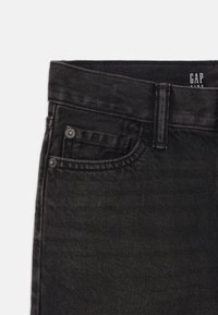 Pantalones de mezclilla negros con un corte recto, que cuentan con un cierre de botón, trabillas para cinturón y un pequeño bolsillo frontal. La etiqueta dice "GAP KIDS."
