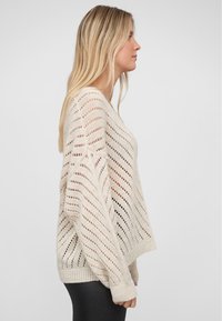 Hellbeige gestrickter Pullover mit lockerer Passform, der offene diagonale Streifen, gerippte Bündchen und einen weiten Rundhalsausschnitt aufweist.
