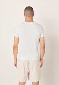 Maglietta bianca a maniche corte con scollo tondo, design aderente, tessuto liscio, abbinata a pantaloncini in velluto a coste beige chiaro.