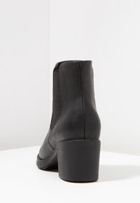 Botín negro de cuero hasta el tobillo con un tacón curvado, paneles laterales elásticos y textura suave, que presenta una punta redondeada y un diseño minimalista.