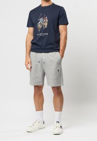 T-shirt en coton bleu marine avec un graphique de match de polo, associé à un short en coton gris. Sneakers blanches, chaussettes blanches jusqu'à la cheville, et une coupe décontractée.
