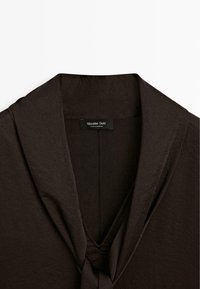 Haut en tissu léger marron avec un col châle, un décolleté en V et un détail noué à l'avant. Comprend une étiquette de marque : Massimo Dutti.