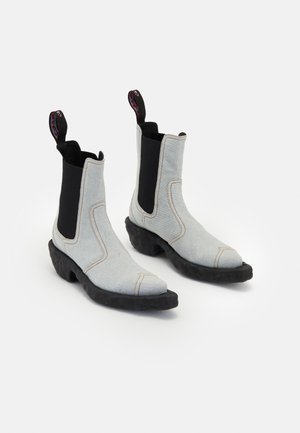 Jasnoszare materiałowe botki za kostkę z czarnymi elastycznymi panelami bocznymi, spiczastymi noskami i teksturowanymi czarnymi gumowymi podeszwami. Posiadają kolorowe pętle do zakupu.