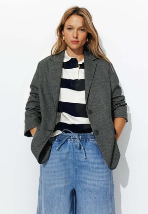 Blazer à motifs gris sur un polo rayé noir et blanc, associé à un short en denim bleu clair à cordon de serrage avec des boutons latéraux.
