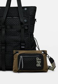 Svart vävd tygväska med texturerade detaljer och justerbara axelremmar, i kombination med en mindre brun påse som har en svart dragkedja.