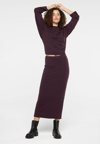 Langes lila Zweiteiler-Outfit aus weichem Stoff, bestehend aus einem kurzärmeligen Oberteil und einem figurbetonten Midirock, kombiniert mit schwarzen Stiefeln.