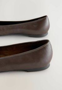Ballerines en cuir marron avec un bout arrondi, texture lisse, couture minimaliste et une semelle plate et basse. Sans embellissements marquants.