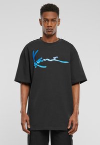 Sort bomulds T-shirt med et stort blåt grafisk design på brystet. T-shirten har en afslappet pasform og korte ærmer.