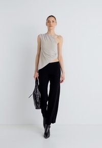 Ασύμμετρο γκρι ανοιχτό τοπ με ντραπέ σχέδιο, συνδυασμένο με μαύρο ριμπ παντελόνι φαρδιάς γραμμής. Το μοντέλο κρατά μια υφασμάτινη τσάντα και φορά κομψές μαύρες μπότες.