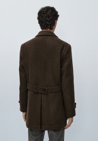 Cappotto marrone in lana con colletto a punte, cintura dietro con bottoni e maniche lunghe; presenta una texture liscia e una vestibilità su misura.