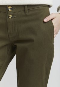 Olive green cotton pants with two button closures, side pockets, and a smooth texture, showing stitching details and a fitted design.