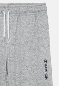 Grijze joggingsbroek van een zachte, textuurstof. Heeft witte trekkoorden en een 'Champion' logo in marineblauw op het linkerpant.