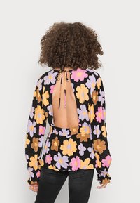 Blusa floral preta com flores rosas, roxas e amarelas. Apresenta um laço nas costas, um design de costas abertas e uma cintura elástica com punhos franzidos.