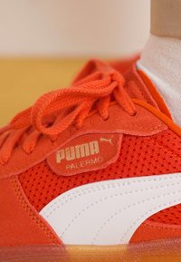 Puma Palermo tenisice s gornjim dijelom od svijetlosmeđeg odstupajućeg materijala, bijelim kožnim akcentima, mrežastim detaljima i zlatnim logom na bočnoj strani.