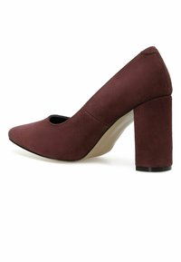Zapato de tacón alto de ante burdeos con punta redonda, diseño con recortes y tacón grueso. Interior suave con suela de contraste.