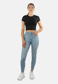 Schwarzes, kurzärmeliges, cropped T-Shirt, kombiniert mit hellblauen, hochtaillierten Skinny-Jeans und weißen Sneakers. Einfaches Design und Passform.