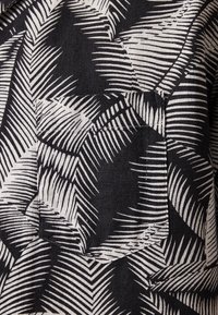 Black fabric featuring a white palm leaf pattern with varying stripe widths, showcasing a textured surface and layered design elements.