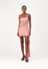 Pink lace dress with a fitted bodice and flowing, asymmetrical hem. Lightweight fabric, adjustable straps, and layered texture.