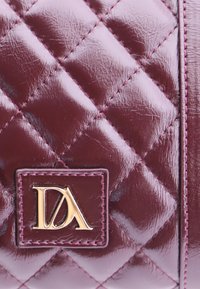 Bolso de mano de cuero acolchado burdeos con acabado brillante, que presenta un logotipo de hardware dorado en un parche rectangular y un contraste de costura rosa.