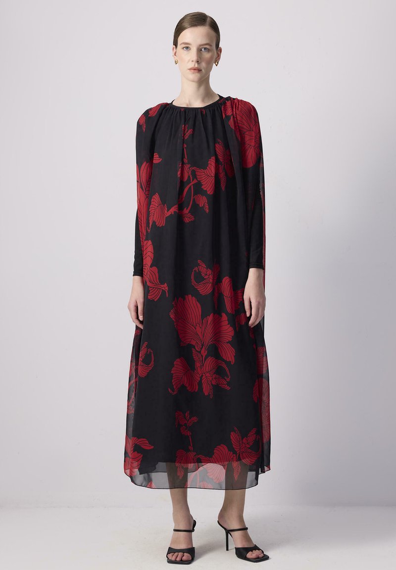 Abito nero a maniche lunghe con stampa floreale rossa, scollo arricciato, silhouette fluida e sovrapposizione trasparente, abbinato a tacchi neri con strappi.