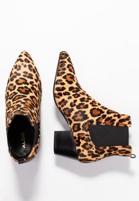 Leopardikuvioiset nilkkurit, joissa on terävä kärki, musta paksu korko, joustavat sivupaneelit ja teksturoitu kangaspinta. Merkki-logo sisäpuolella.